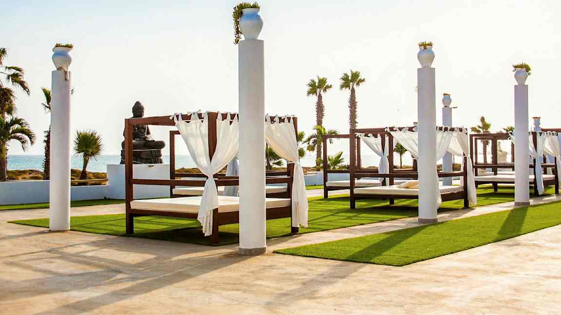 Utomhusmiljö med baldakinsängar och staty vid havet. (AI-genererad text)