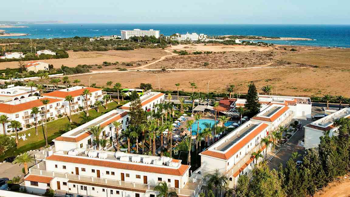 Flygfoto över ett hotellområde med pool och havet i bakgrunden. (AI-genererad text)