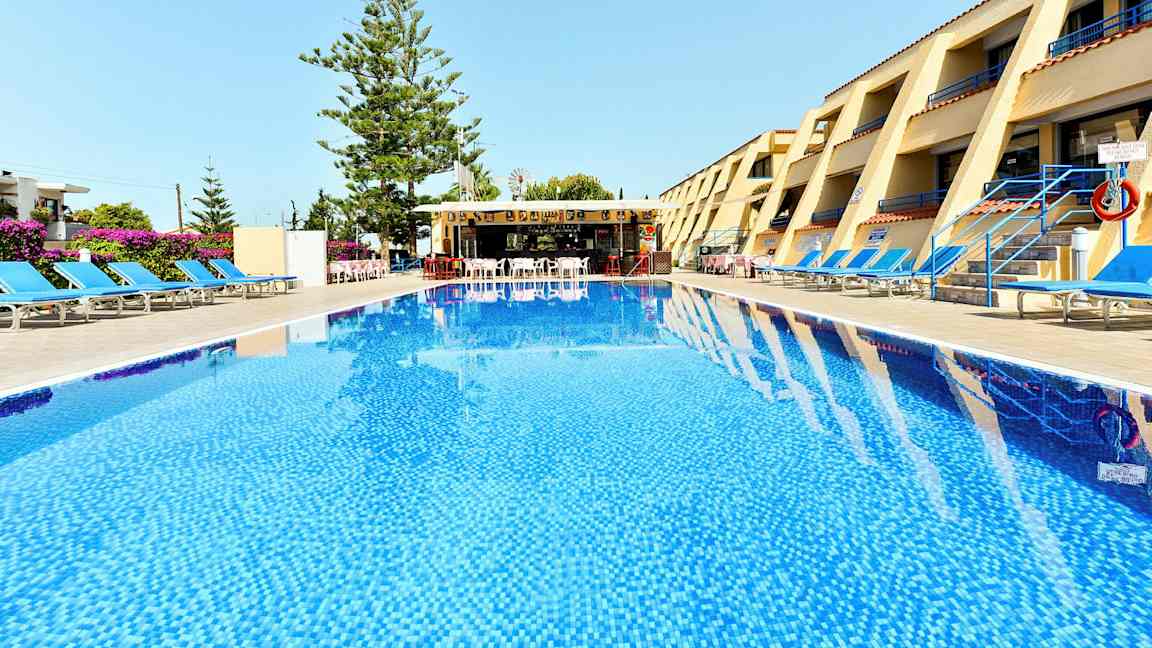 Ett hotellområde med en pool i förgrunden, solstolar på båda sidor och en bar i bakgrunden. (AI-genererad text)