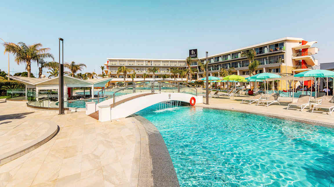 Bild av en pool, med en liten bro och hotellbyggnad i bakgrunden. (AI-genererad text)