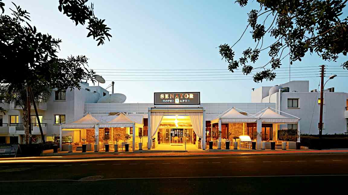 Entrén till Senator Hotel Apartments med kvällsbelysning. (AI-genererad text)