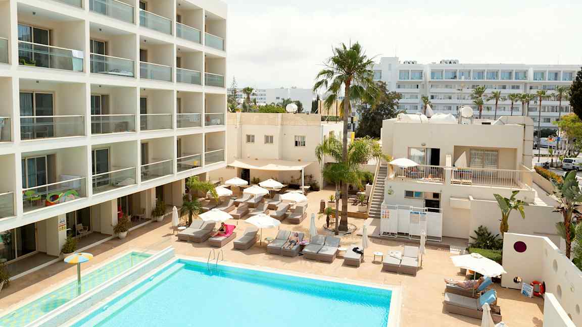 Hotellområde med pool, solstolar och byggnader. (AI-genererad text)