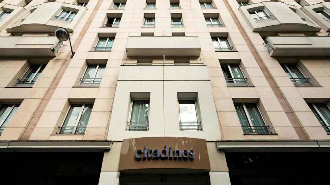 Fasad av byggnad med skylten 'Citadines' och flera fönster. (AI-genererad text)