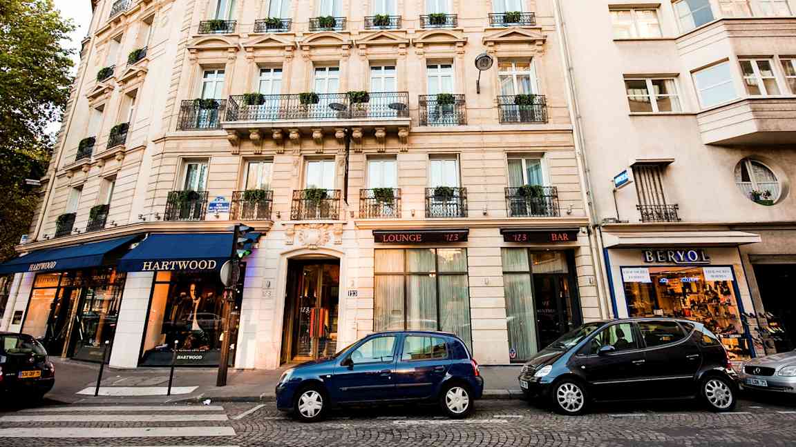 Ett flerbostadshus med butiker och parkerade bilar framför. (AI-genererad text)