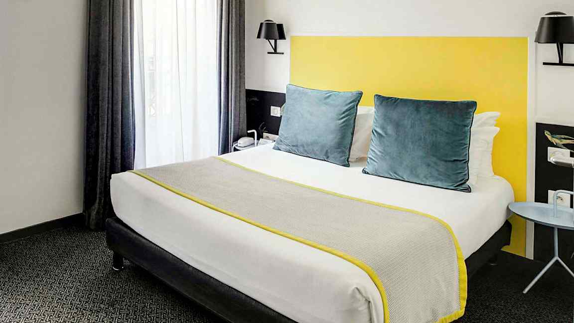 Ett hotellrum med en säng utrustad med grå och gula detaljer. (AI-genererad text)