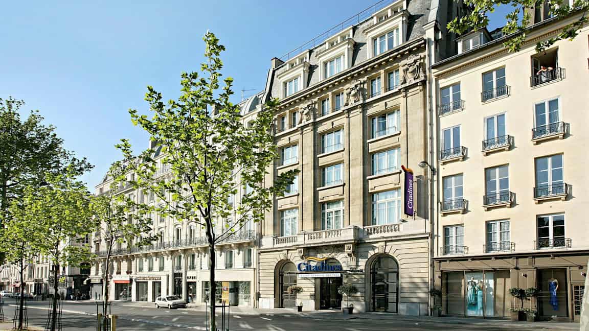 En gata med byggnader, träd och människor vid ett soligt väder. (AI-genererad text)