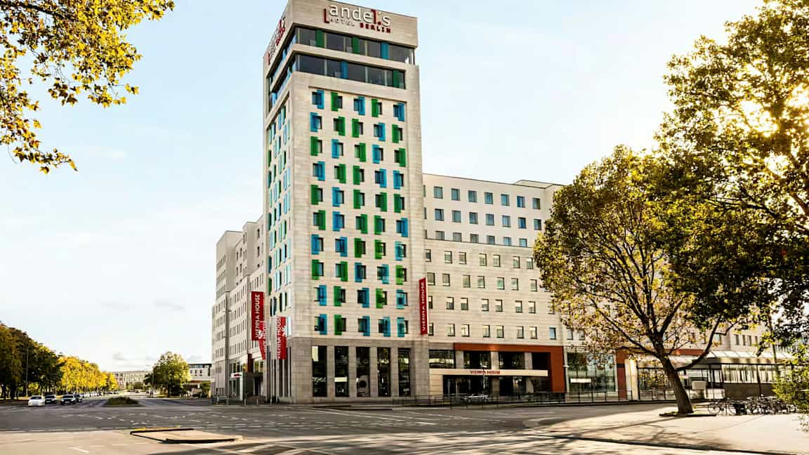 En modern hotellbyggnad med vit fasad och färgade fönster, omgiven av vägar och träd. (AI-genererad text)