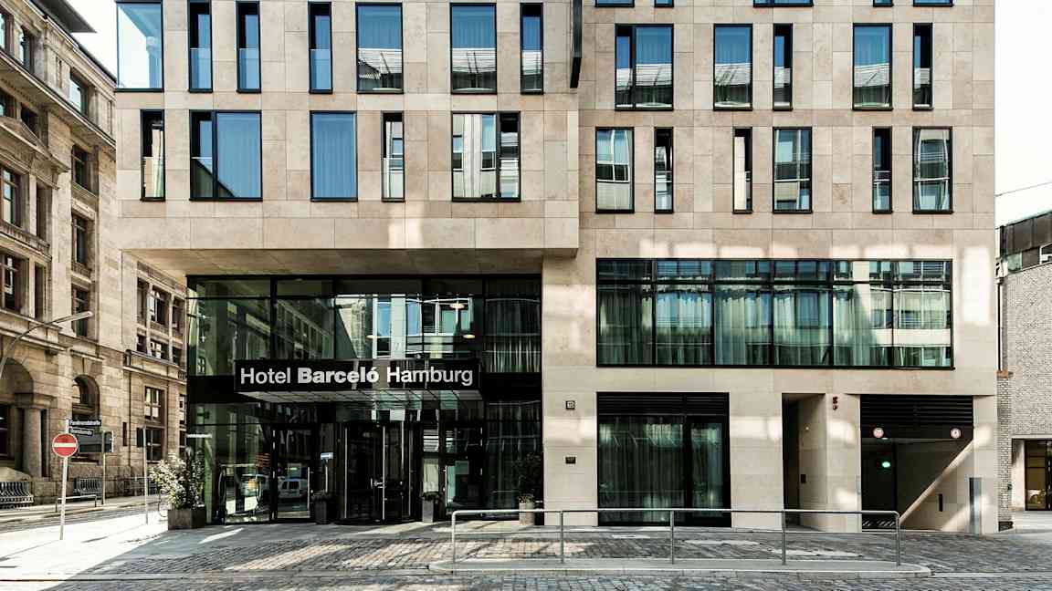 En byggnad med modern fasad och en entré där det står "Hotel Barceló Hamburg". (AI-genererad text)