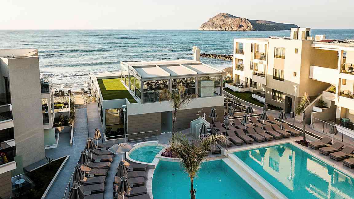 Hotellbyggnader med pool och solstolar nära havet. (AI-genererad text)