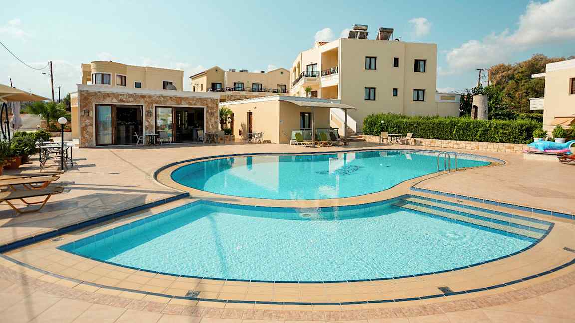 En bild som visar en utomhuspool omgiven av solstolar och byggnader i bakgrunden. (AI-genererad text)