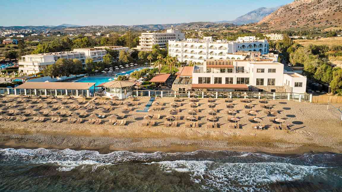 Ett hotellkomplex vid stranden med poolområde, solstolar, parasoller och en terrass med utsikt över havet. (AI-genererad text)