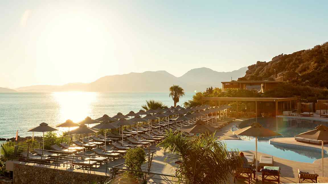 Solnedgång vid havet där solstolar och parasoller står vid en pool och en terrass. (AI-genererad text)