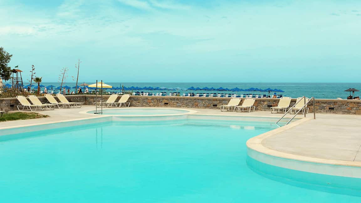 En pool med solstolar, och i bakgrunden havet med parasoll. (AI-genererad text)