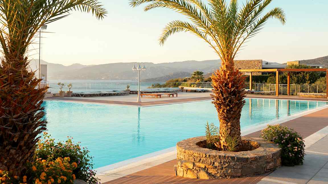 Solnedgång över en pool med palmer och blommor vid poolkanten. (AI-genererad text)