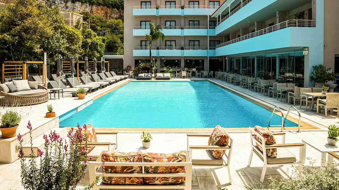 En utomhuspool omgiven av solstolar och parasoller vid ett modernt hotell. (AI-genererad text)