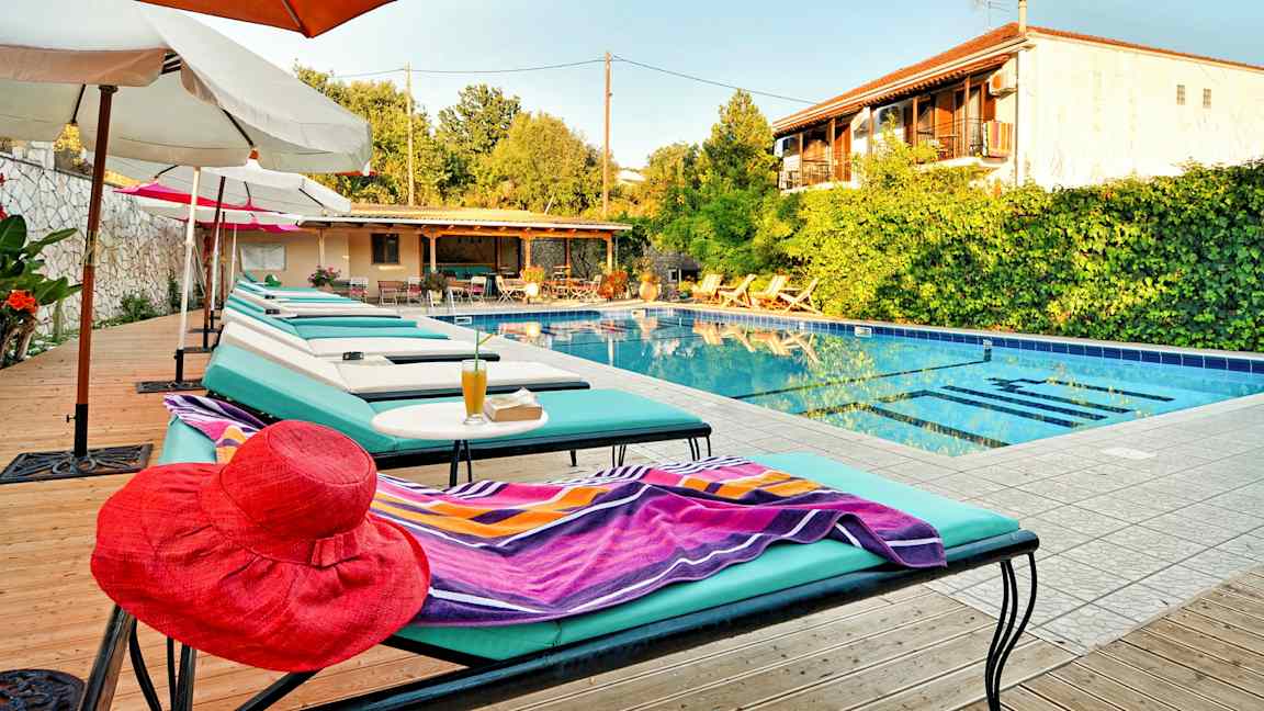 Solstolar vid en pool med parasoller, en röd hatt och handduk synligt. (AI-genererad text)