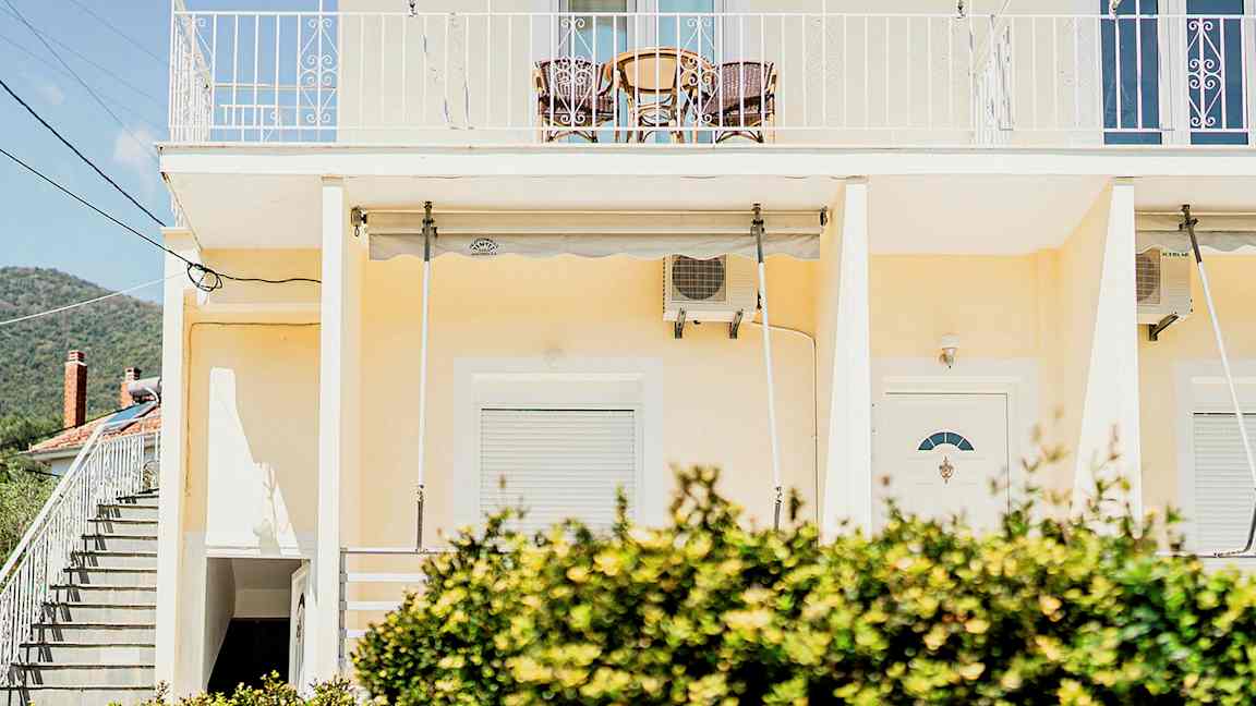 En gul byggnad med en balkong högst upp och buskar i förgrunden. (AI-genererad text)