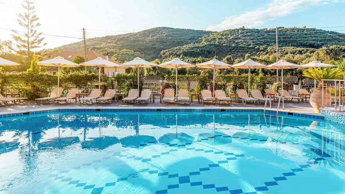 Pool med solstolar och parasoller framför en grön bergsutsikt. (AI-genererad text)
