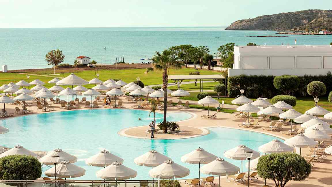 En pool med solstolar och parasoll, med utsikt mot havet och en grönskande omgivning. (AI-genererad text)