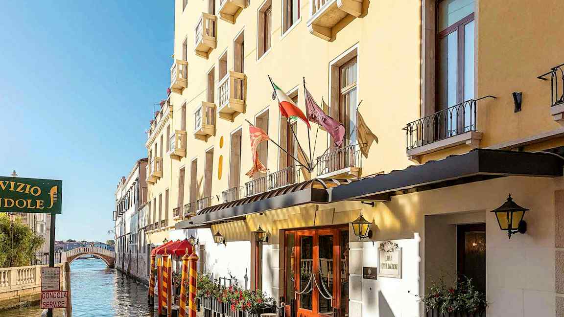 En gul byggnad med balkonger längs en kanal, med en gångbro i bakgrunden. (AI-genererad text)