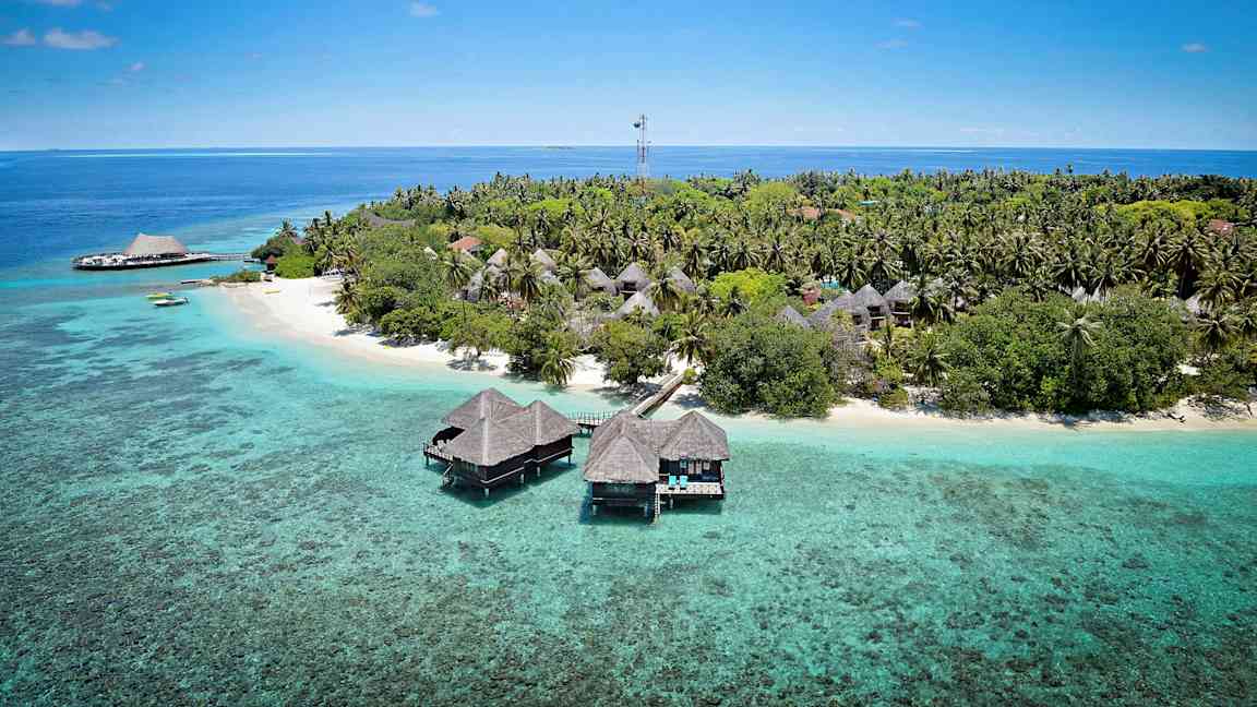 En tropisk ö med träbungalows på pålar över det turkosa vattnet och omgiven av grönska. (AI-genererad text)