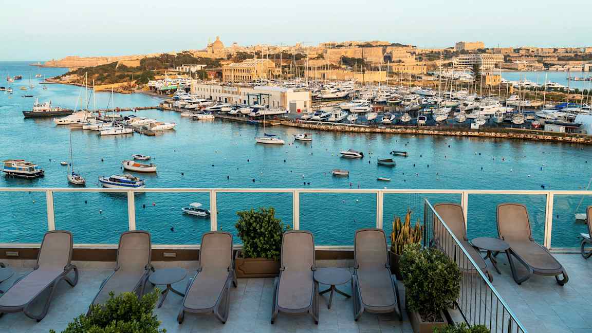 Vy över en marina med båtar och en terrass med solstolar. (AI-genererad text)