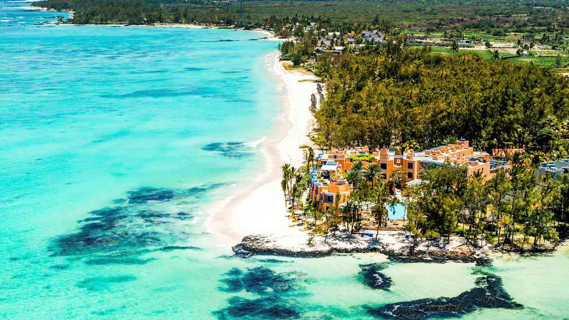 En sandstrand med turkost vatten och hotell omgivna av grönska. (AI-genererad text)