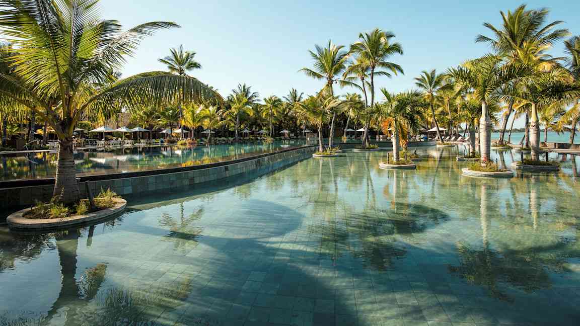 En stor swimmingpool omgiven av palmer under en klarblå himmel. (AI-genererad text)