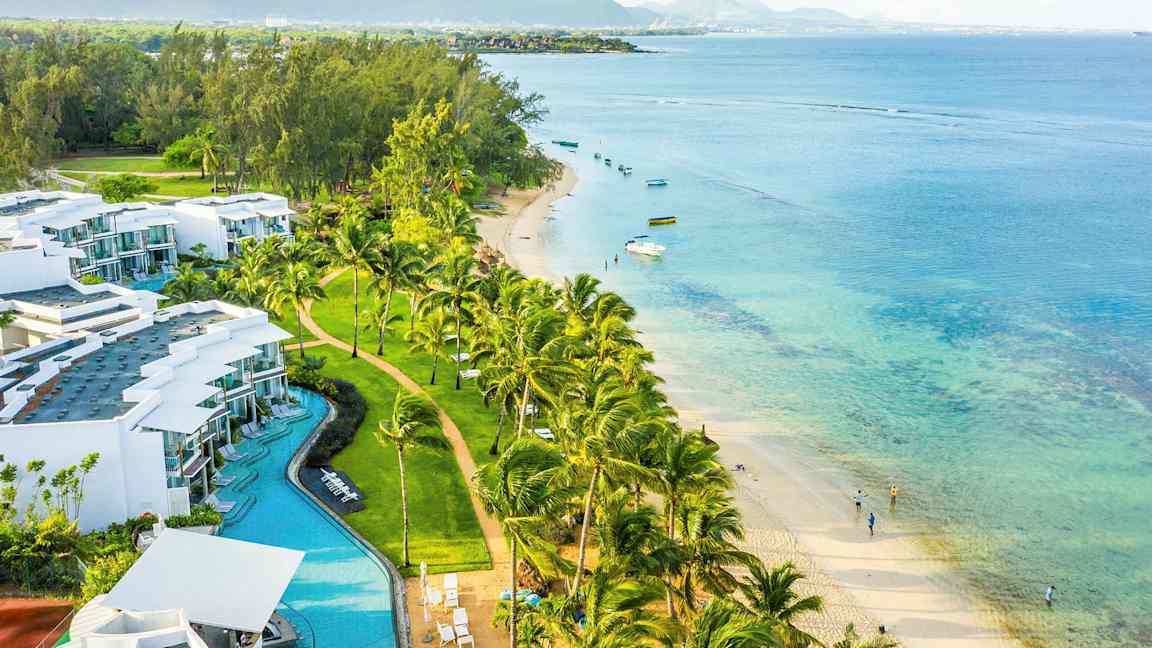 Ett kustlandskap med vita byggnader, palmer, sandstrand och turkost hav. (AI-genererad text)