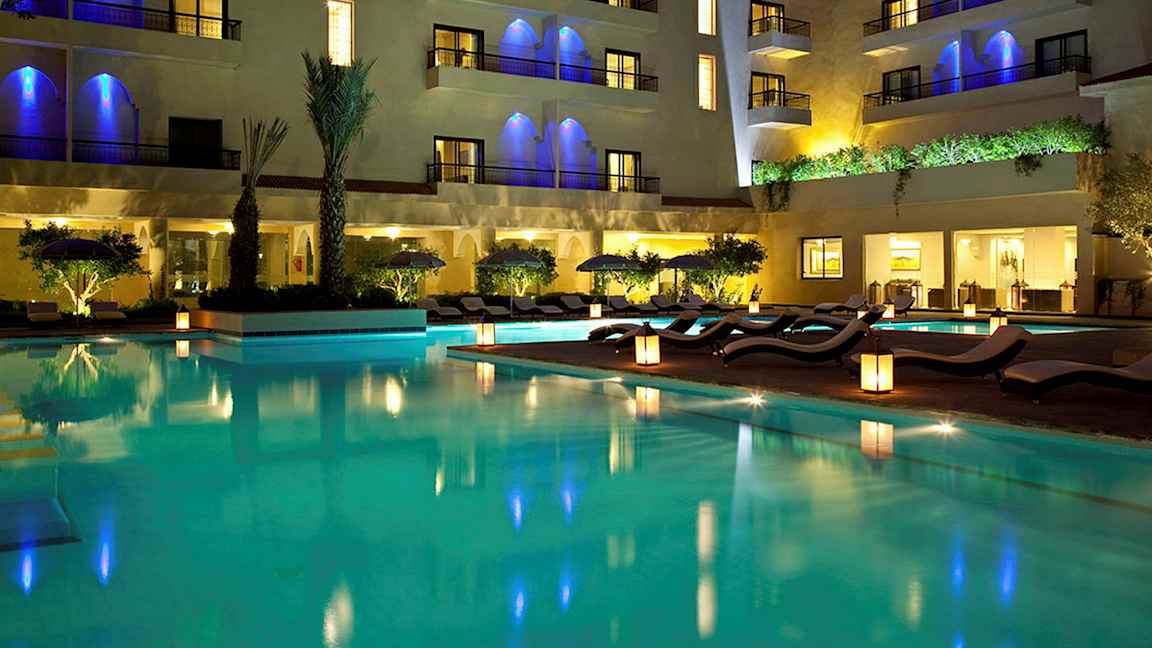En vacker hotellpool med stolar och belysning på kvällen. (AI-genererad text)