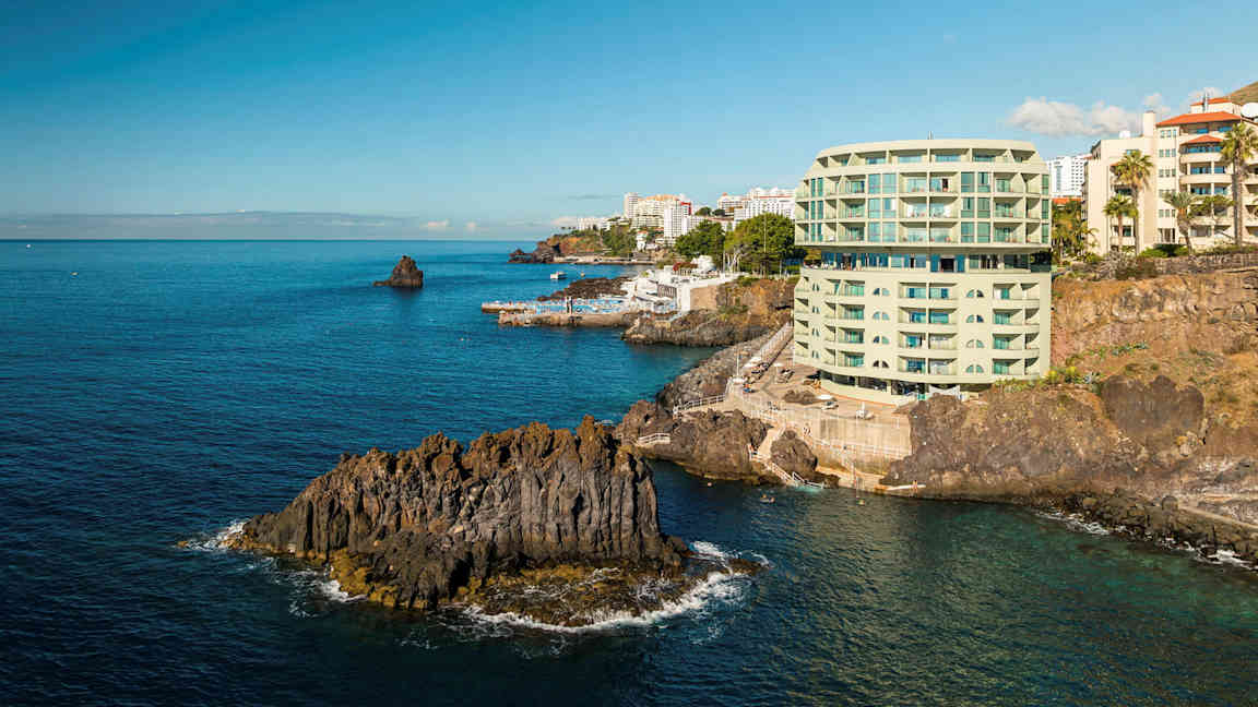 Ett hotell vid havet med klippformationer och klarblå himmel. (AI-genererad text)