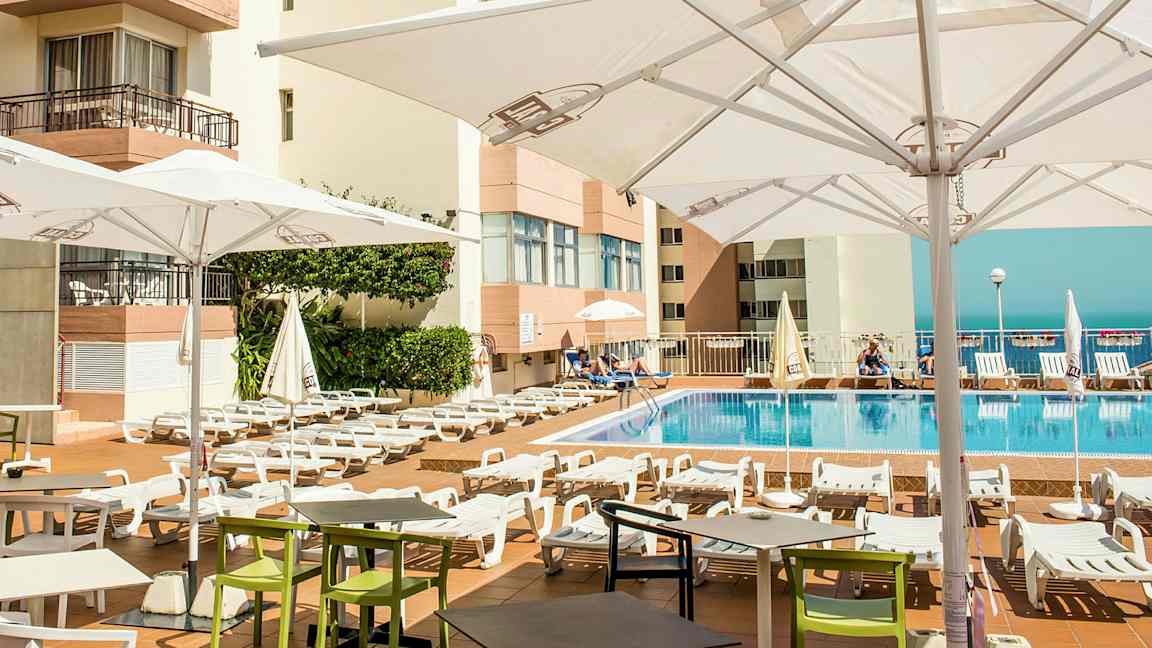 Utomhuspoolområde med solstolar och parasoller vid ett hotell. (AI-genererad text)