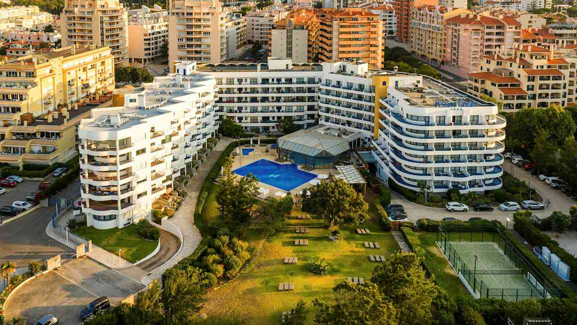 Hotell med pool och kringliggande trädgårdsområden i ett stadslandskap. (AI-genererad text)