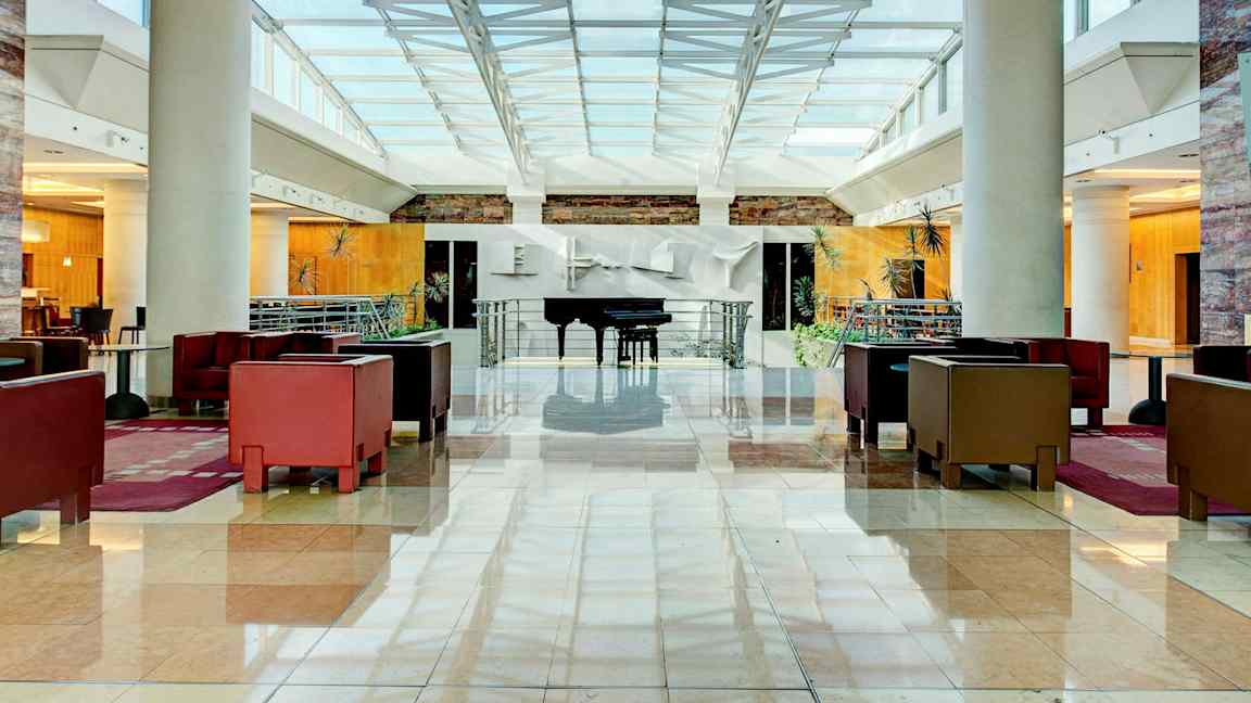 Ljus och rymlig hotellobby med sittgrupper och ett piano. (AI-genererad text)