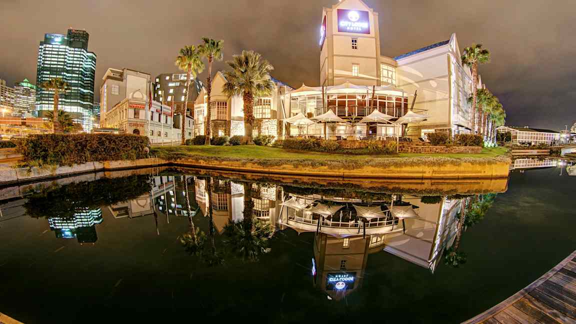 Hotell och byggnader vid en vattenkanal på natten med spegelreflektioner i vattnet. (AI-genererad text)