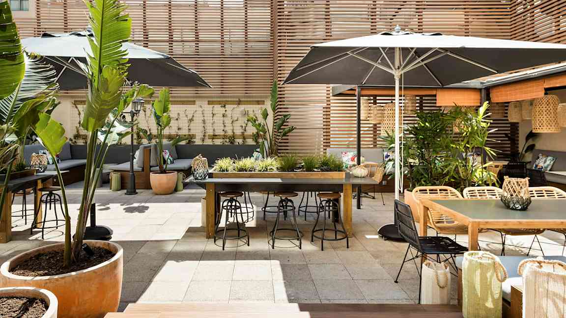 En utomhus terrass med bord, stolar och växtdekorationer, omgiven av träpaneler. (AI-genererad text)