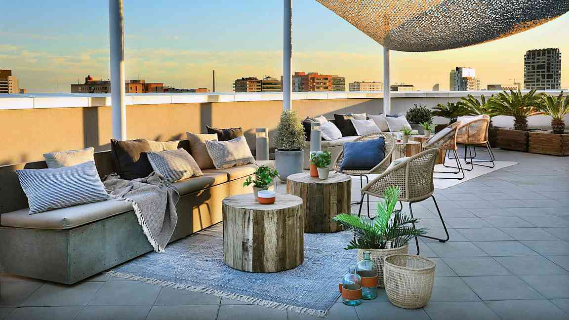 En takterrass med sittmöbler, bord och korgar dekorerade med växter och kuddar är avbildad. (AI-genererad text)