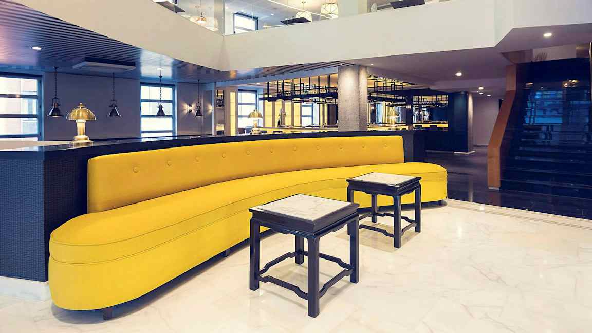 Ett stilfullt inrett utrymme med en gul soffa, små bord och modern belysning. (AI-genererad text)