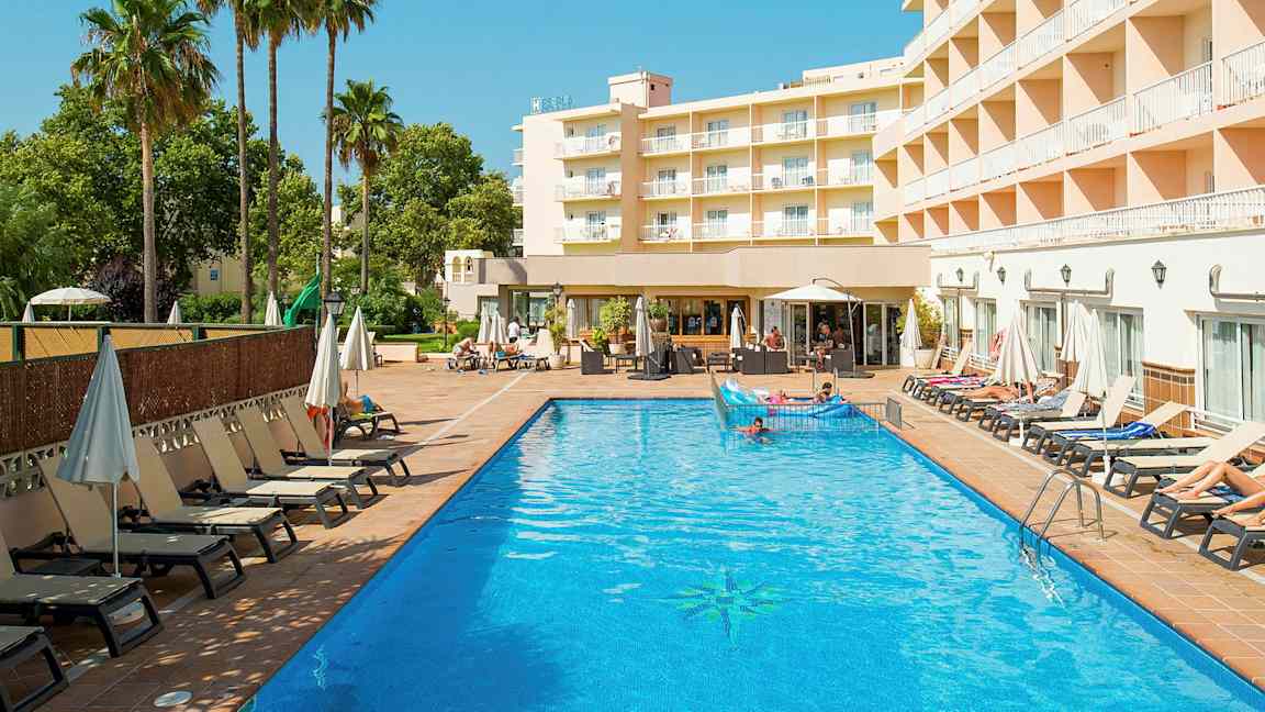 En hotellbyggnad syns bredvid en utomhuspool med solstolar och parasoller runt omkring. (AI-genererad text)