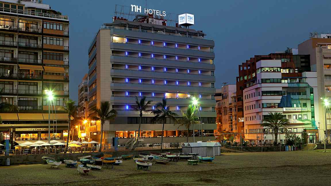 Bild av ett hotell vid havet på kvällen, med ljusskyltar och omgivande byggnader. (AI-genererad text)