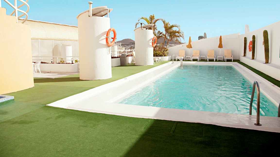 En utomhuspool ligger på en takterrass med solstolar och parasoller runt omkring. (AI-genererad text)