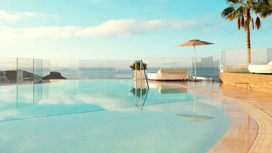 En infinitypool med utsikt över havet, omgiven av solsängar och palmer. (AI-genererad text)