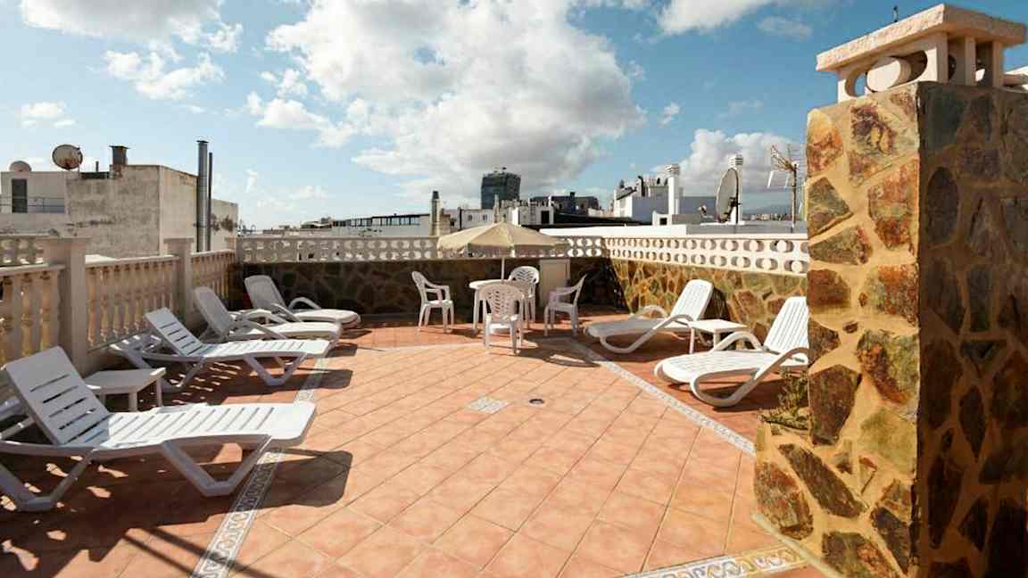 Solstolar och ett bord med stolar på en terrass med utsikt över byggnader. (AI-genererad text)