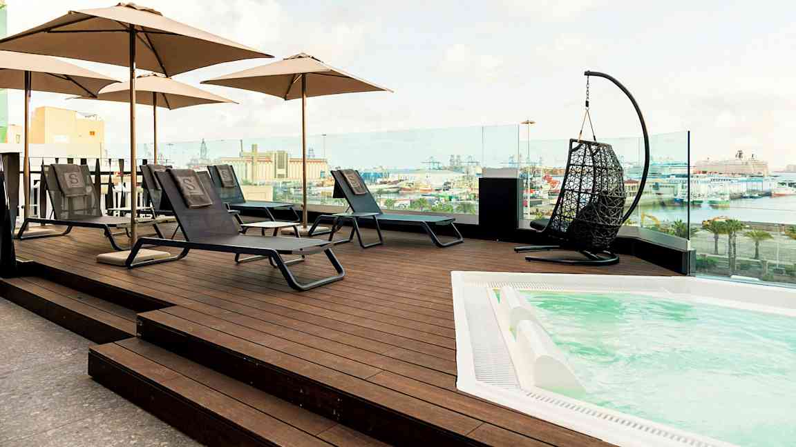 Takterrass med liggstolar, parasoll och bubbelpool, utsikt över en hamn. (AI-genererad text)