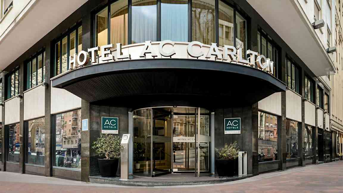 En hotellfasad med skylttexten "HOTEL AC CARLTON" synlig ovanför ingången. (AI-genererad text)