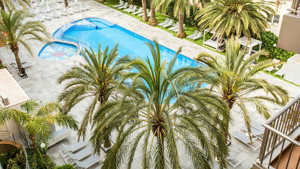 En swimmingpool med solstolar och palmer runt omkring. (AI-genererad text)