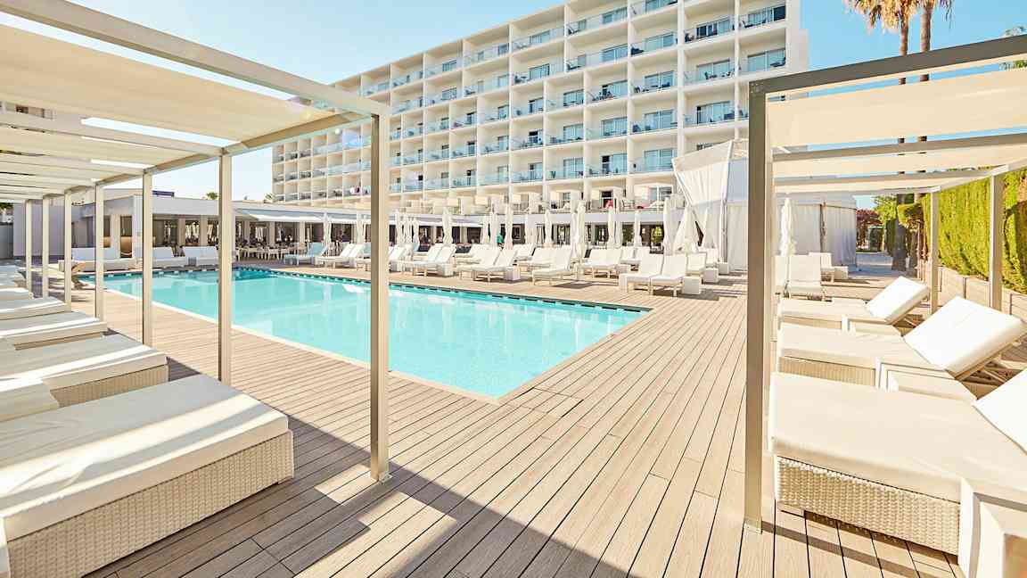 En modern hotelldesign med en pool omgiven av solstolar och parasoller, med ett stort vit byggnad i bakgrunden. (AI-genererad text)