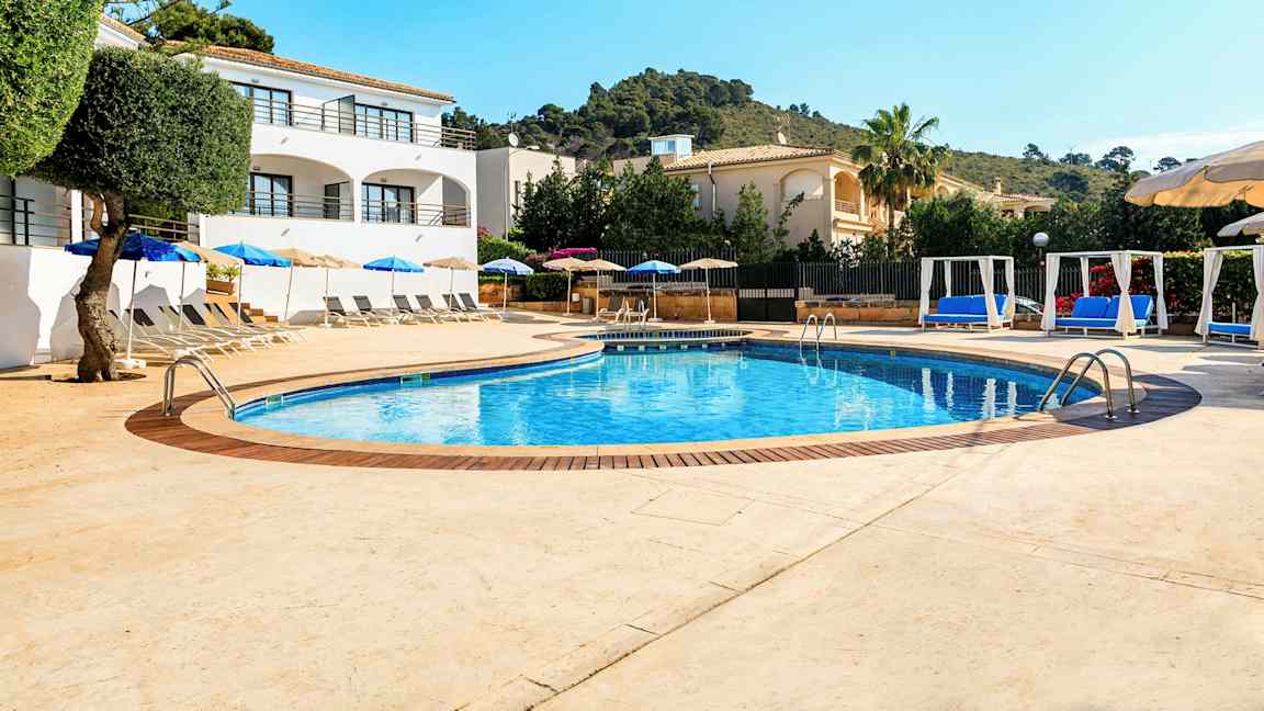 Poolområde med solstolar och parasoller samt omgivande byggnader. (AI-genererad text)