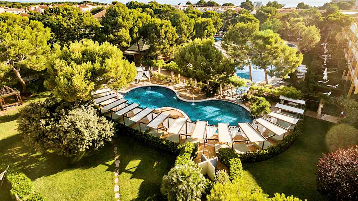 Bild av en kurvig pool med omgivande solstolar och grönska, med en vy över bebyggelse och hav i bakgrunden. (AI-genererad text)