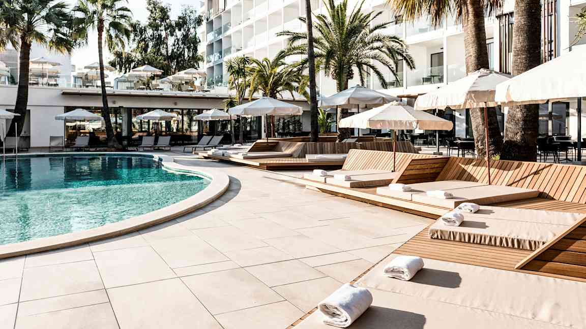 En pool omgiven av solstolar och parasoller vid ett hotell, med palmer i bakgrunden. (AI-genererad text)